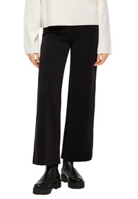 Zwarte wijde broek gemaakt van een glad materiaal, met een hoge taille en subtiele stiksels, in combinatie met zwarte enkellaarzen.