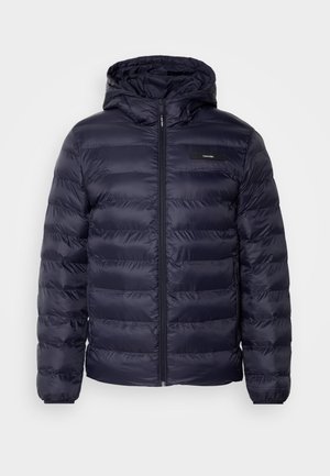 Giacca puffer blu navy con cappuccio, caratterizzata da cuciture orizzontali, una cerniera centrale e una piccola etichetta con logo sul lato superiore sinistro.