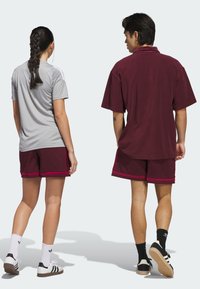 Gray athletic shirt with short sleeves, paired with maroon shorts featuring mesh texture and contrasting hem. Black and white shoes complete the look.
