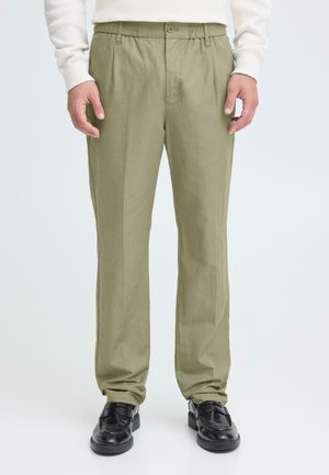 Hellgrüne Hose mit lockerem Schnitt, elastischem Bund, Knopfverschluss und glatter Textur, kombiniert mit schwarzen Schuhen.