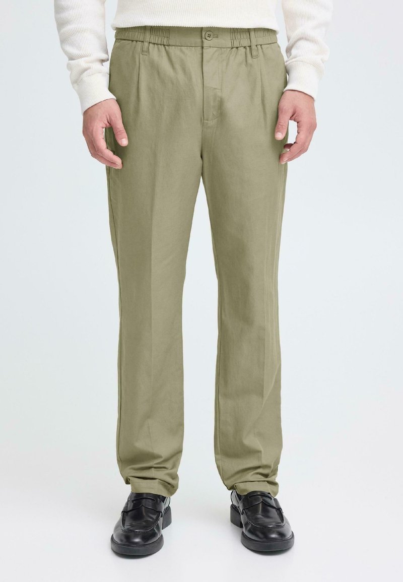 Ανοιχτό πράσινο παντελόνι με χαλαρή γραμμή, ελαστική μέση, κούμπωμα με κουμπί και ομαλή υφή, συνδυασμένο με μαύρα παπούτσια.