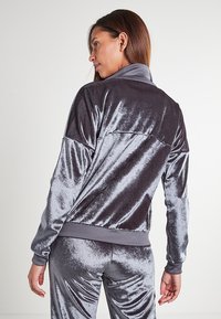 Giacca da track in velour grigia con colletto alto, polsini a costine e una texture morbida e lucida. Progettata con pannelli contrapposti sulle spalle.