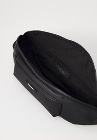 Zwarte Calvin Klein tas met een gladde, gestructureerde buitenkant, voorzien van een rits hoofdcompartiment en een extra ritsvak.