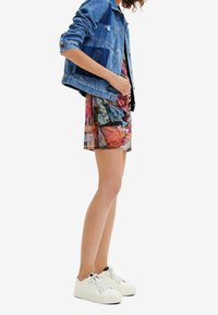 Denim jacket with distressed details, multi-colored patterned dress, and white sneakers with black accents; shown from the side.