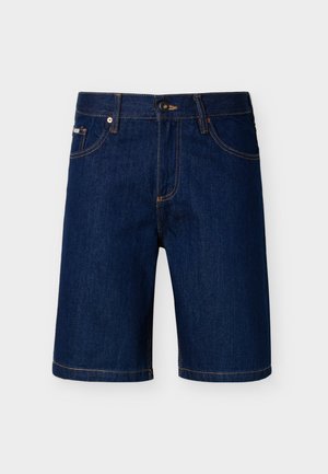 Donkerblauwe denimshorts met vijf zakken, knoopsluiting en gele stiknaden, afgebeeld tegen een effen lichtgrijze achtergrond.