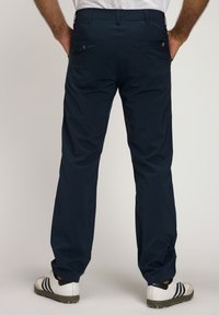 Pantaloni blu navy con texture liscia, dotati di tasche posteriori e fit classico. Abbinati a scarpe da ginnastica bianche.