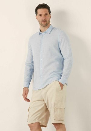 Camisa de botones de manga larga en azul claro, confeccionada con una tela texturada, combinada con pantalones cortos de cargo beige con bolsillos laterales y un corte relajado.