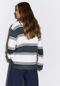 Prugasta majica dugih rukava u tamnosivoj i bijeloj boji s horizontalnim prugama; mekan materijal, širok kroj, okrugli izrez na vratu i blago spuštena ramena.