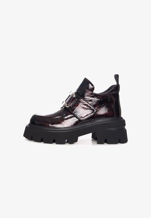 Bottines noires à plateforme épaisse avec une finition bordeaux en vernis, présentant une boucle sur le côté et une tige texturée. Semelle en caoutchouc solide avec de profondes rainures.