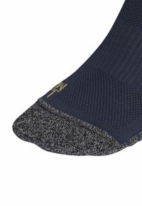 Tamno plava čarapa s teksturiranim gornjim dijelom, sive uzorke na prstima i zlatnim logotipom u blizini gležnja. Materijali uključuju mješavinu pamuka za udobnost.