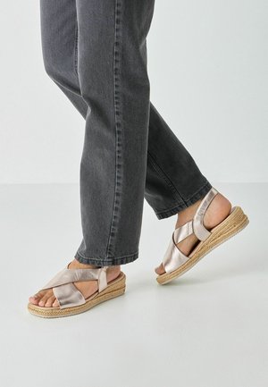 Metalliske roseguld espadrille-sandaler med krydsremme og kilehæl indpakket i jute. Bruges med mørkegrå, tilspidsede jeans.