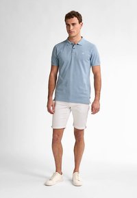 Světlě modré polo tričko s krátkými rukávy a zapínáním na knoflíky, vyrobené z bavlny, v kombinaci s bílými džínovými šortkami a krémovými teniskami.