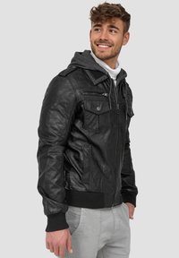 Black leather jacket with multiple zippered pockets, ribbed cuffs, and a gray hooded lining, styled with a smooth texture and fitted design.