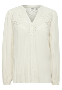 Blouse beige clair en tissu texturé, avec un panneau en dentelle décoratif au niveau de la poitrine, fermeture à boutons et manches longues avec des poignets froncés.