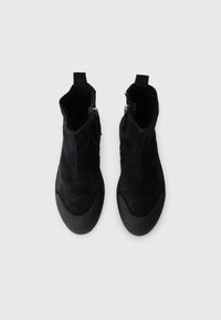 Bottines noires en cuir suédé, avec un dessus lisse, une semelle en caoutchouc robuste et des fermetures éclair sur les côtés pour un enfilage facile.