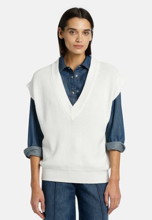 White knitted sleeveless sweater with a V-neckline, featuring textured fabric and ribbed trim, layered over a denim button-up shirt.