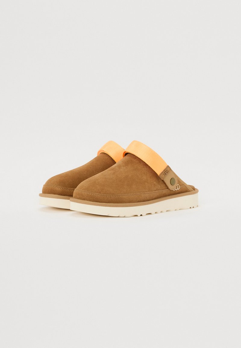 Scarpe slip-on in suede marrone con una ampia fascia arancione, suola crema, punta arrotondata e texture liscia. Nessun motivo visibile o dettagli hardware.
