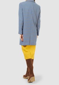 Modrý a bílý sako s motivem ptičí stopy, žlutá pletená sukně po kolena a hnědé semišové vysoké boty se silnou podrážkou.