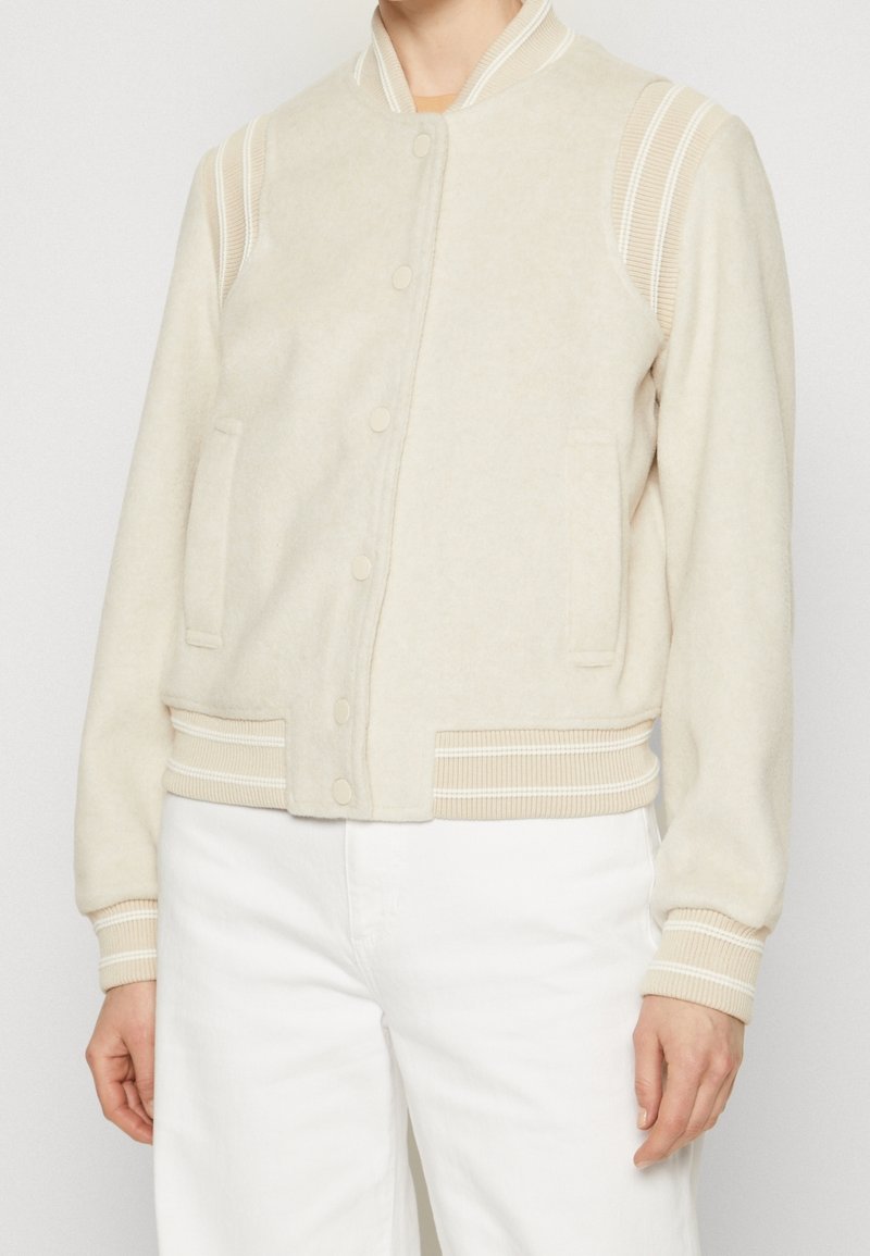 Blouson aviateur couleur crème en mélange de laine douce, avec poignets et col côtelés, fermeture à boutons-pression, et poches latérales.