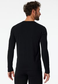 Maglietta nera a maniche lunghe con taglio dritto, colletto tondo e texture di cotone liscia. Presenta cuciture minime e una silhouette aderente.