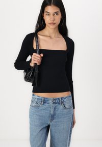 Black ribbed long-sleeve top with a square neckline, paired with light blue denim jeans. Model holding a small black bag.