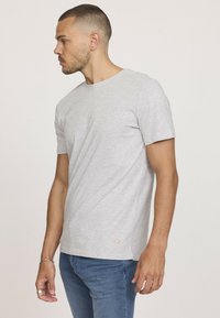 T-shirt en coton gris à manches courtes, col rond, et un petit accent en diamant orange près de l'ourlet. Silhouette ajustée.