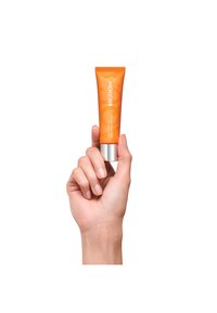 Appelsinkrem i en hånd med sølvfarget bunn, merket "AQUASOURCE Vitamin Glow Gel." Glatt tekstur, minimalistisk design og livlig farge.