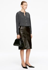 Graues Hemd, glänzender schwarzer Lederbleistiftrock, schwarze Handtasche und schwarze spitze Slingback-Pumps. Glatte Texturen und strukturierte Formen.