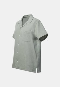 Chemise vert clair à manches courtes avec boutons, une seule poche poitrine et un motif de tissu texturé sur un fond uni.
