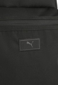 Mochila de tela negra con una superficie texturizada, un compartimento con cremallera y un parche del logo de PUMA en negro. Diseño liso y resistente.