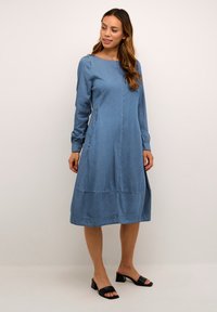 Denim kleita ar garām piedurknēm, apaļu kakla izgriezumu un izplestu siluetu. Ar kontrastējošiem diegiem un krīt zem ceļgaliem.