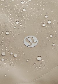 Tela beige con gotas de agua, con un logotipo plateado. La textura es suave con un ligero brillo, lo que indica resistencia al agua.