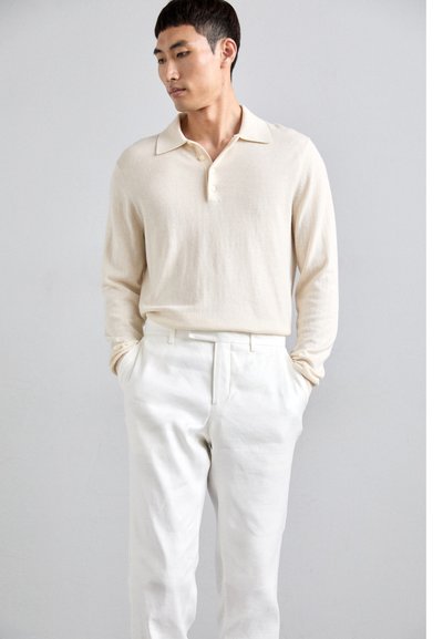 Cremefarvet langærmet polo shirt med krave og tre knapper, parret med hvide bukser. Blød tekstur, minimalistisk design.