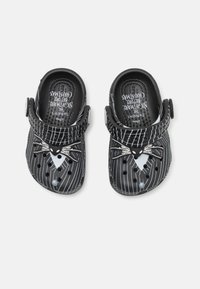 Black plastic clogs with white pinstripe design. Features a character face with whiskers. Includes ventilation holes and adjustable strap.