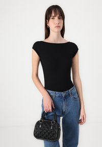 Black ribbed bodysuit with a wide neckline, paired with blue high-waisted jeans. Holding a black textured handbag with double handles.