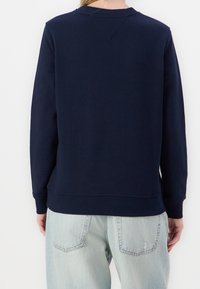 Navy blue sweatshirt with ribbed cuffs and hem. Soft fabric, crew neckline, and minimal stitching detail. Worn with light blue denim jeans.