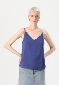 Camisola blu con colletto a scalloped e spalline sottili, realizzata in tessuto leggero, abbinata a una gonna di jeans. Presenta una vestibilità rilassata.