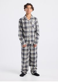 Checked flannel pajama set in navy, white, and beige. Button-up shirt with chest pocket, loose-fitting pants with an elastic waistband.