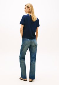 Μπλε ναυτικό βαμβακερό t-shirt, άνετη εφαρμογή, σε συνδυασμό με ανοιχτό μπλε τζιν με φαρδιά μπατζάκια. Ξυπόλητος με απλά μαύρα σανδάλια, μινιμαλιστικό και casual στυλ.