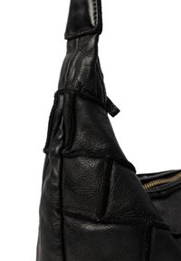 Angolo di una borsa in pelle nera con cuciture visibili, superficie testurizzata e parziale cerniera dorata su sfondo bianco.