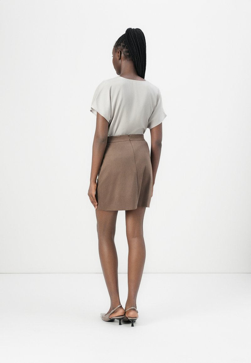 Falda marrón con una textura suave y un diseño ajustado, combinada con una blusa de manga corta gris claro, vista desde atrás.