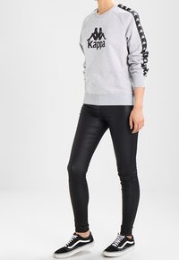 Felpa grigia con logo nero e strisce a contrasto, abbinata a leggings neri e sneaker bianco e nere. Texture liscia in tutto.