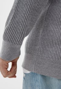 Grauer ribbeliger Pullover mit strukturiertem Strick, im lässigen Schnitt mit enganliegenden Bündchen, kombiniert mit hellblauer Denim.