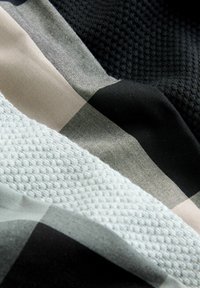Tyger med rutigt mönster i beige, svart och vitt, med en texturerad nätstruktur och slät yta, som framhäver olika material och färger.