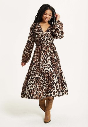Leopard-print midi dress featuring long sleeves, a wrap design, a tiered skirt, and a tied waist, paired with brown cowboy boots.