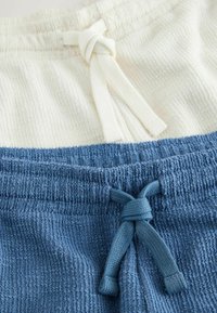 Gros plan sur des shorts en tissu texturé avec taille élastique et cordons noués, un en crème et un en bleu.