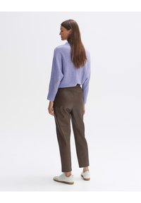 Lichtpaarse, oversized trui met ribgebreide manchetten, gecombineerd met getailleerde bruine broek. Witte sneakers met gestructureerde details maken de outfit compleet.