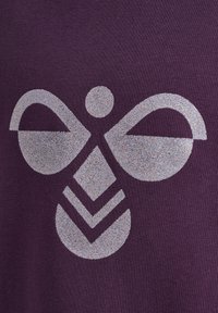 Mörkt lila tyg har en central grafik med en stiliserad bi-design i silverglitter, som visar geometriska former och mjuka linjer.
