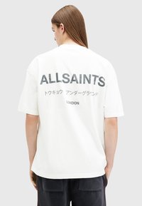 White oversized t-shirt with black text on the back, displaying “ALLSAINTS” and Japanese characters, made of cotton material.