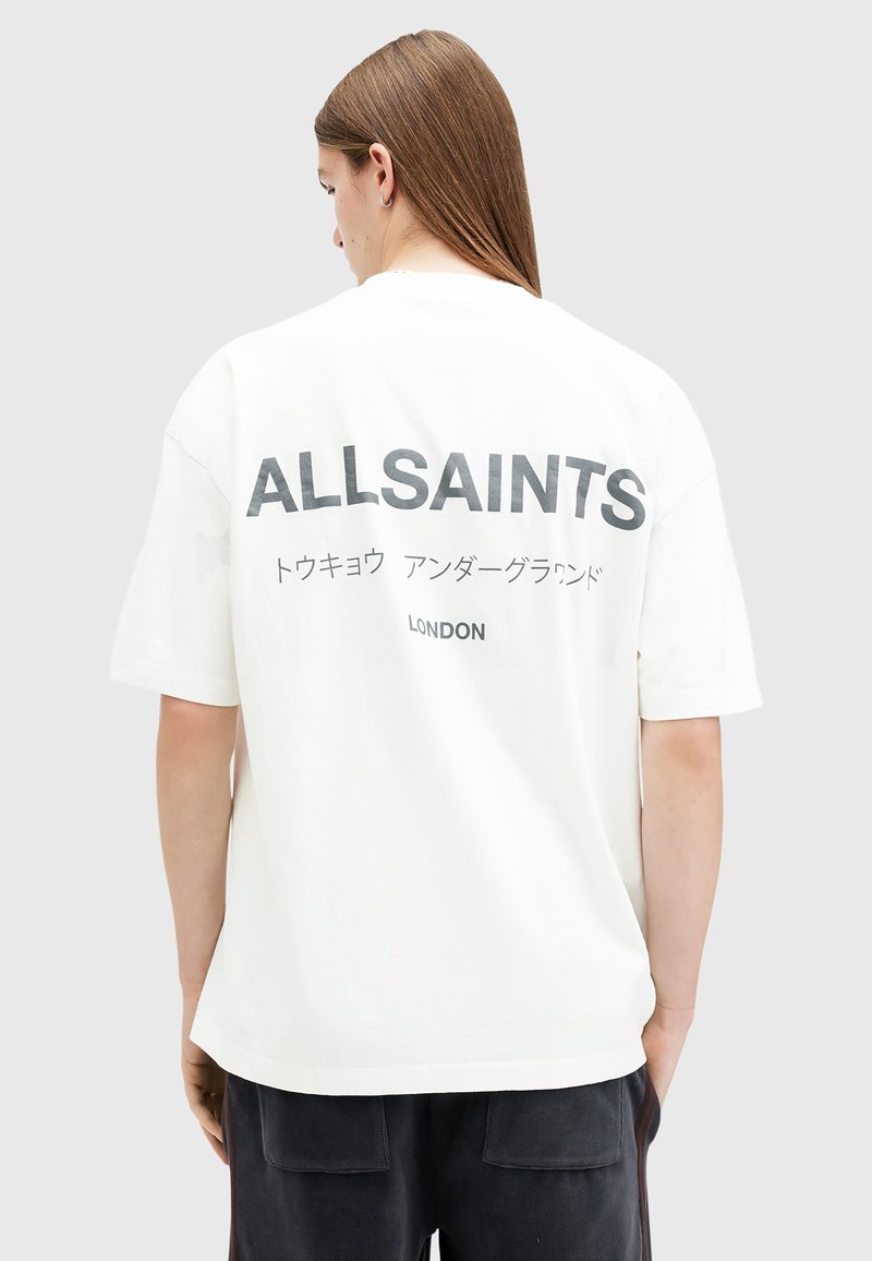 White oversized t-shirt with black text on the back, displaying “ALLSAINTS” and Japanese characters, made of cotton material.